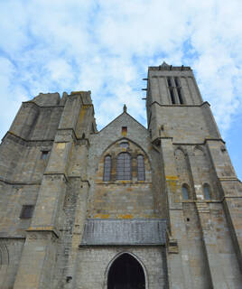 La majestueuse Cathédrale Saint-Samson à Dol-de-Bretagne, une imposante structure gothique en pierre avec une tour clocher et des arches, sous un ciel nuageux.