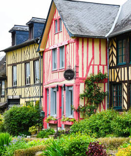 Des maisons à pans de bois colorées et traditionnelles à Dol-de-Bretagne, avec des détails architecturaux et des jardins fleuris devant, sous un ciel clair.