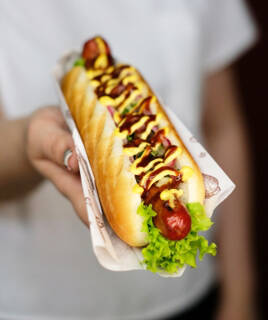 Un hot-dog garni de saucisse, salade, oignons et de deux types de moutarde, tenu dans une main, typique des repas rapides que l'on peut trouver à Europa-Park.