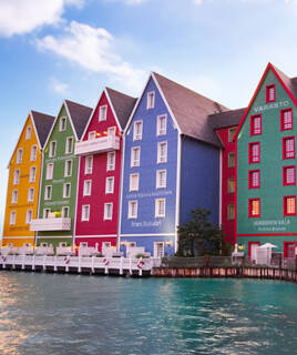 Les façades colorées de maisons de style nordique, jaunes, vertes, rouges et bleues, reflétant l'architecture d'un quartier d'Europa-Park, bordent un canal sous un ciel clair de fin de journée.