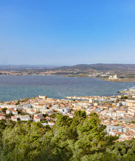 Une vue panoramique depuis le Mont Saint-Clair à Frontignan, dominant la ville, l'Étang de Thau et la Méditerranée, avec des collines lointaines sous un ciel bleu clair.