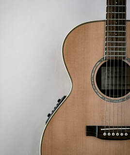 Une guitare acoustique en bois clair, en gros plan sur le côté droit de l'image, évoquant l'univers musical du Musée Georges Brassens à Sète, près de Frontignan.