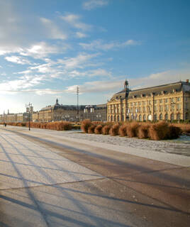 La Place de la Bourse à Bordeaux en Gironde, avec ses élégants bâtiments du 18e siècle reflétant la lumière du soleil matinal, bordant le quai avec des parterres de végétation.