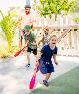 Des enfants joyeux participant à une activité en extérieur, probablement au club enfant d'un camping près d'Aix-en-Provence, courant avec des bâtons de jeu sous la surveillance d'un animateur.