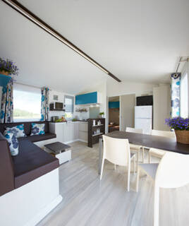 L'intérieur spacieux et moderne d'un mobil-home, comme ceux disponibles dans un camping près d'Aix-en-Provence, avec un coin salon, une cuisine équipée et un espace repas, décoré de touches bleues et florales.