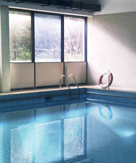 Une piscine intérieure calme aux Thermes de Gréoux-les-Bains, avec un anneau de sauvetage rouge et blanc sur le bord, et des reflets de lumière sur l'eau bleue, évoquant un espace de détente.