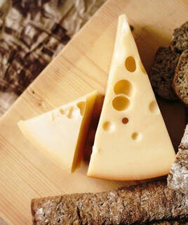 Une part de fromage suisse avec ses trous caractéristiques, accompagnée de pain de seigle sur une planche en bois, évoquant les spécialités culinaires des environs du Lac Léman.
