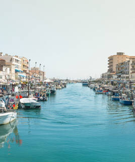 Le canal de Palavas-les-Flots, près de Lattes, avec de nombreux bateaux de pêche et de plaisance amarrés le long des rives, bordé par des bâtiments de la ville sous un ciel clair.