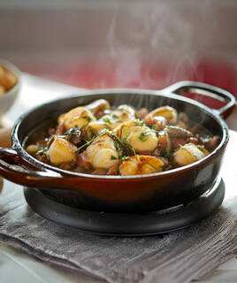 Une bouilleture, spécialité de Loire-Atlantique, présentée dans une cocotte en fonte fumante, garnie de noix de Saint-Jacques, de champignons et d'herbes aromatiques.