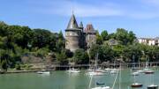 Le Château de Pornic en Loire-Atlantique, une imposante bâtisse médiévale avec ses toits coniques, domine un port rempli de bateaux de plaisance, entouré de verdure sous un ciel bleu.