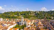 Une vue aérienne d'Agen, en Lot-et-Garonne, avec la Cathédrale Saint-Caprais dominant les toits de la ville, bordée par des collines verdoyantes et le Lot en arrière-plan, sous un ciel bleu parsemé de nuages blancs.