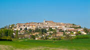 Le village médiéval de Monflanquin en Lot-et-Garonne, perché sur une colline et entouré de champs verdoyants, sous un ciel bleu clair.