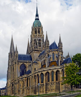 La majestueuse Cathédrale Notre-Dame de Bayeux, avec sa flèche élancée et ses toits en ardoise sombre, sous un ciel nuageux.
