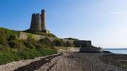 La Tour Vauban de Saint-Vaast-la-Hougue dans la Manche, une forteresse médiévale imposante sur un promontoire verdoyant surplombant la mer, sous un ciel bleu.