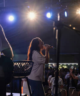 Une chanteuse sur scène avec un micro, éclairée par des projecteurs, interprétant une chanson lors d'un festival ou concert à Merlimont, avec une foule en arrière-plan.