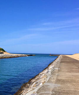 L'embouchure du courant de Mimizan, près de Messanges, avec des digues en pierre et un chenal menant à l'océan Atlantique, sous un ciel bleu clair.