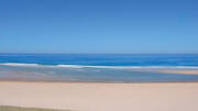 La vaste plage de sable de Messanges, avec des vagues douces s'écrasant sur le rivage et l'océan Atlantique s'étendant à l'horizon sous un ciel bleu clair et dégagé.