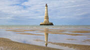 Le majestueux Phare de Cordouan, près de Montalivet, se dressant dans l'océan Atlantique et se reflétant sur le sable mouillé à marée basse, sous un ciel nuageux.