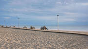 Une longue plage de sable à Montalivet, avec une promenade en bois et des bancs, sous un ciel légèrement nuageux, et une personne assise près d'un vélo au bord de l'océan.