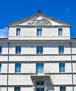 Façade imposante du Musée Fabre à Montpellier, avec son architecture classique, ses nombreuses fenêtres et un fronton orné d'un bas-relief et d'une horloge sous un ciel bleu éclatant.