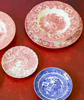 Des assiettes en faïence de Moustiers-Sainte-Marie, avec des motifs traditionnels rouges et bleus, posées sur une surface rouge, évoquant le savoir-faire du Musée de la Faïence.