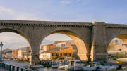 Le Vallon des Auffes à Marseille, en Provence-Alpes-Côte d'Azur, avec son pont en pierre à plusieurs arches enjambant le petit port de pêche où sont amarrés des bateaux, et des maisons colorées le long de l'eau, sous un ciel clair.