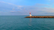 Un petit phare rouge et blanc au bout d'une jetée rocheuse à Carnon, près de Palavas-les-Flots, se dressant dans la mer Méditerranée sous un ciel légèrement nuageux au lever ou coucher du soleil.