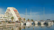 Le port de plaisance de La Grande-Motte, à proximité de Palavas-les-Flots, avec ses célèbres bâtiments pyramidaux et de nombreux bateaux amarrés sous un ciel bleu éclatant.