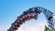 Des passagers dans les wagons d'une montagne russe bleue, le Silver Star, réalisant une inversion à Europa-Park en Allemagne, sous un ciel bleu clair.
