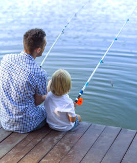 Un homme et un enfant pêchant ensemble depuis un ponton en bois sur un plan d'eau douce, évoquant une activité de camping et de pêche.
