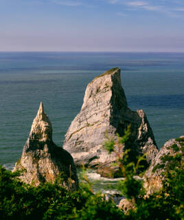 Les impressionnants rochers de la Pointe du Bile à Pénestin, se dressant dans l'océan avec une végétation dense au premier plan, sous un ciel bleu clair.