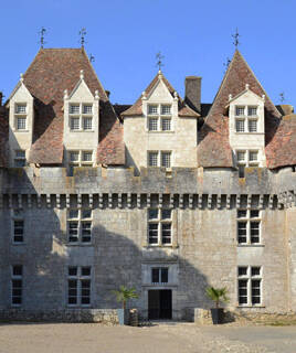 Façade en pierre du Château de Monbazillac, en Périgord, avec ses lucarnes et toits de tuiles, sous un ciel bleu.