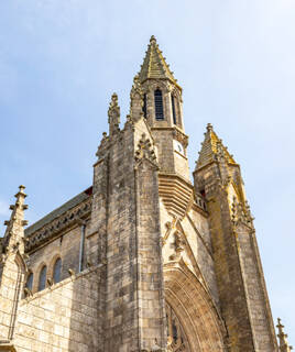 La façade gothique de la Collégiale Saint-Aubin de Guérande, près de Piriac-sur-Mer, avec ses tours et pinacles en pierre et ses vitraux, s'élevant vers un ciel bleu clair.