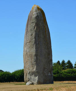 Un grand menhir se dressant dans un champ près de Guérande, non loin de Piriac-sur-Mer, sous un ciel bleu clair avec quelques nuages.