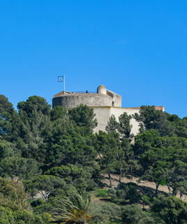 Le Fort Sainte-Agathe, une forteresse historique, trônant au sommet d'une colline boisée sur l'île de Porquerolles, sous un ciel bleu intense.