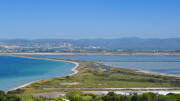 Vue aérienne de la Presqu'île de Giens près de Porquerolles, montrant la double-tombolo avec les plages de l'Almanarre et les salins, sous un ciel bleu dégagé, avec la ville d'Hyères et les montagnes en arrière-plan.