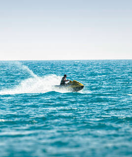 Une personne faisant du jet-ski sur les eaux bleues de la Méditerranée à Port Grimaud, laissant un sillage d'écume derrière elle, sous un ciel clair.
