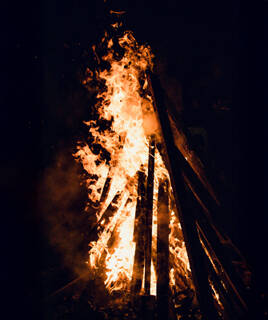 Un grand feu de joie s'élevant dans la nuit, avec des flammes oranges et rouges, rappelant les Feux de la Saint-Jean, une fête traditionnelle à Port Grimaud.