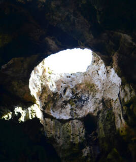 L'ouverture circulaire du ciel vue depuis l'intérieur de la Grotte des Fées à Port Leucate, laissant passer un puits de lumière sur les parois rocheuses sombres de la grotte.