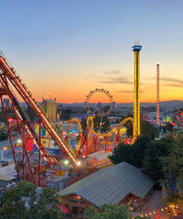 Le parc d'attractions Europark à Vias, près de Portiragnes, illuminé au crépuscule avec ses montagnes russes, sa grande roue et ses tours d'attractions brillant sous un ciel orangé.