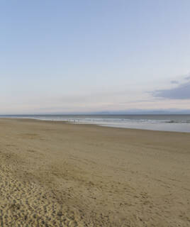 La longue plage de sable de Saint-Gilles-Croix-de-Vie, s'étendant à l'infini vers l'océan, sous un ciel pâle de fin de journée.