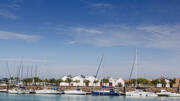 Le port de plaisance de Saint-Gilles-Croix-de-Vie, avec de nombreux voiliers amarrés et des bâtiments blancs aux toits rouges bordant le quai, sous un ciel bleu éclatant.