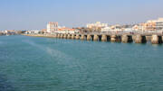 Les Sables d'Olonne, près de Saint-Gilles-Croix-de-Vie, avec un estacade s'avançant dans l'eau et la ville côtière en arrière-plan sous un ciel bleu clair.