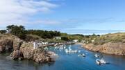 Le port de l'Île d'Yeu, près de Saint-Hilaire-de-Riez, une crique rocheuse abritant de nombreux bateaux de pêche et de plaisance, entourée de végétation et de petites maisons, sous un ciel bleu parsemé de nuages blancs.