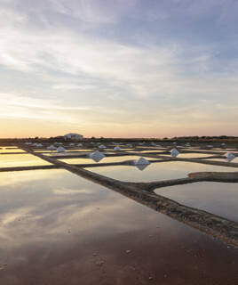 Des carreaux d'eau des Marais Salants de Saint-Hilaire-de-Riez reflétant le ciel au coucher du soleil, avec des monticules de sel blanc prêts à être récoltés.