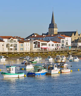Le port de Saint-Gilles-Croix-de-Vie, près de Saint-Hilaire-de-Riez, avec des bateaux de pêche et de plaisance flottant sur l'eau, et le clocher de l'église du village dominant les maisons blanches en arrière-plan.