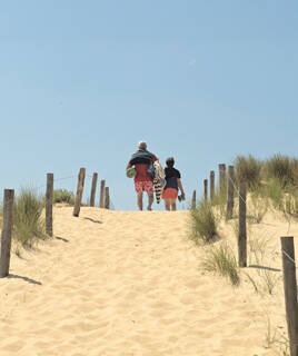 Deux personnes montant un sentier sablonneux bordé de dunes et de piquets en bois, menant probablement au Sentier Littoral à Saint-Hilaire-de-Riez, sous un ciel bleu clair.