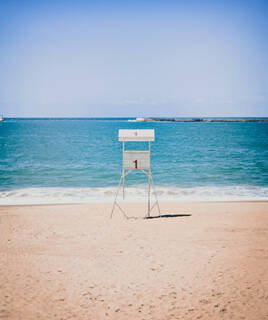 Une chaise de surveillance de sauveteur solitaire sur la plage de Saint-Jean-de-Luz, face à l'océan Atlantique, sous un ciel bleu clair.