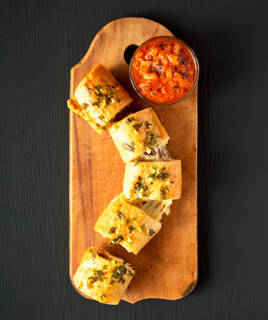 Un préfou, spécialité vendéenne de Saint-Jean-de-Monts, tranché et garni d'ail et de persil, est servi sur une planche en bois avec un ramequin de sauce tomate.