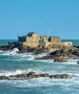 Le Fort National de Saint-Malo, une forteresse en pierre se dressant sur un îlot rocheux battu par les vagues, sous un ciel bleu éclatant.